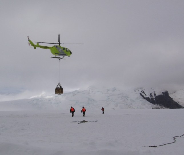 DAP helicopter running a sling load over a glacier