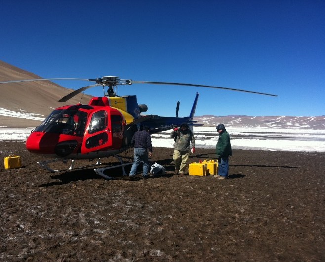 DAP helicopter crew loading gear in the field, snowline behind