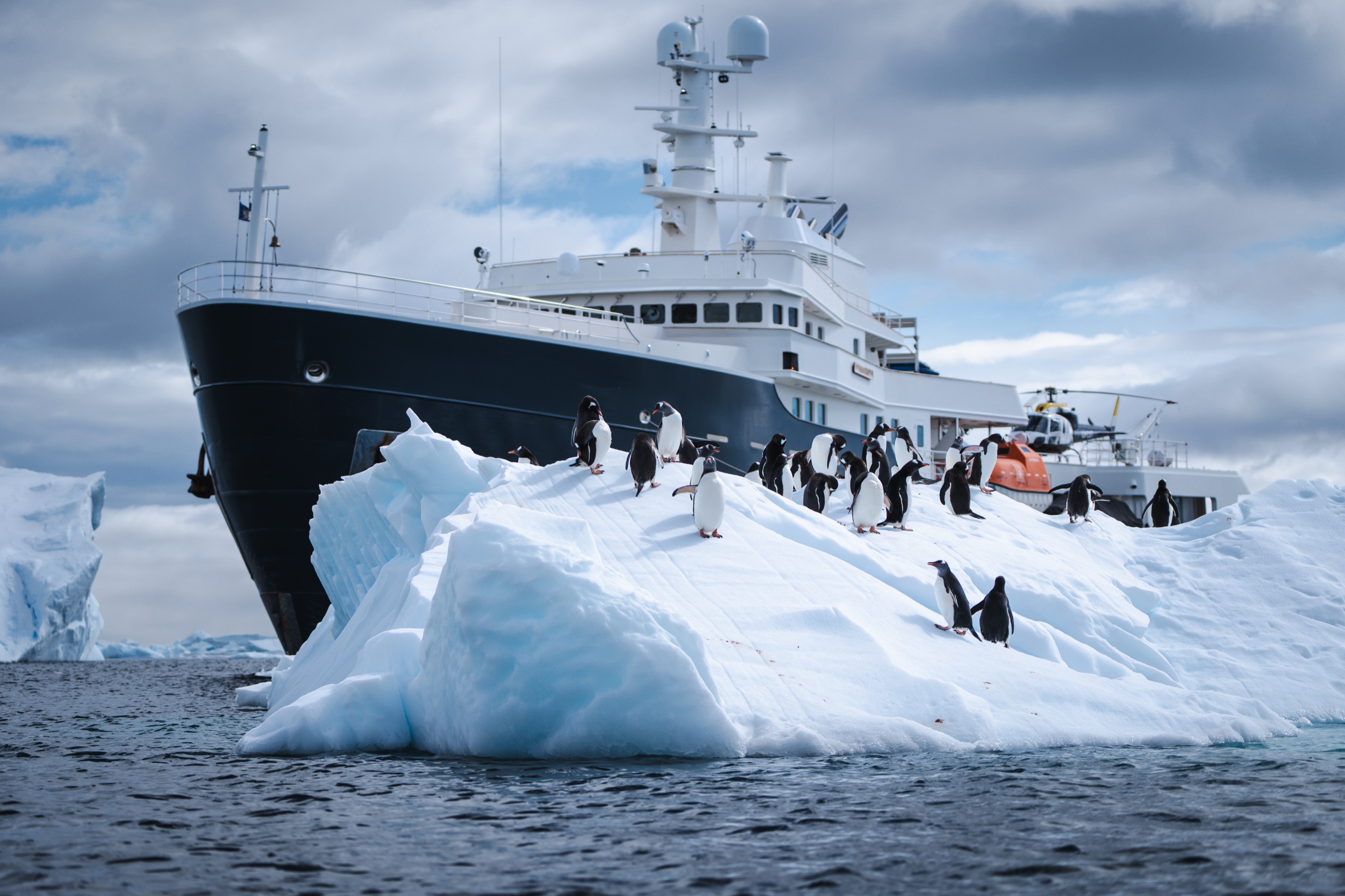 M/Y Legend at the ice edge with penguins on an iceberg and a helicopter aboard, Antarctic Peninsula