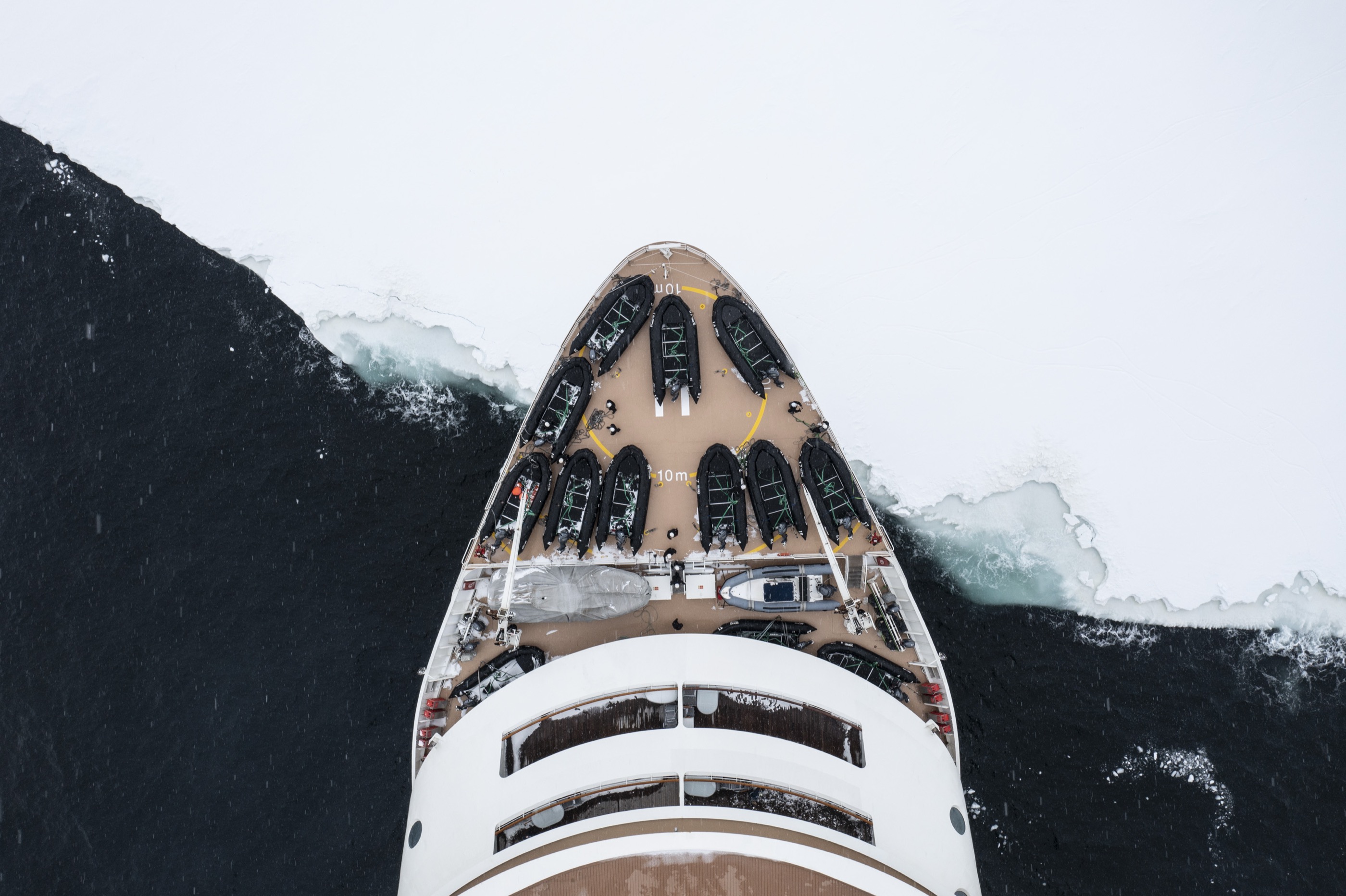 Top-down of an explorer vessel bow ranged with tenders, cutting through sea ice, Ross Sea